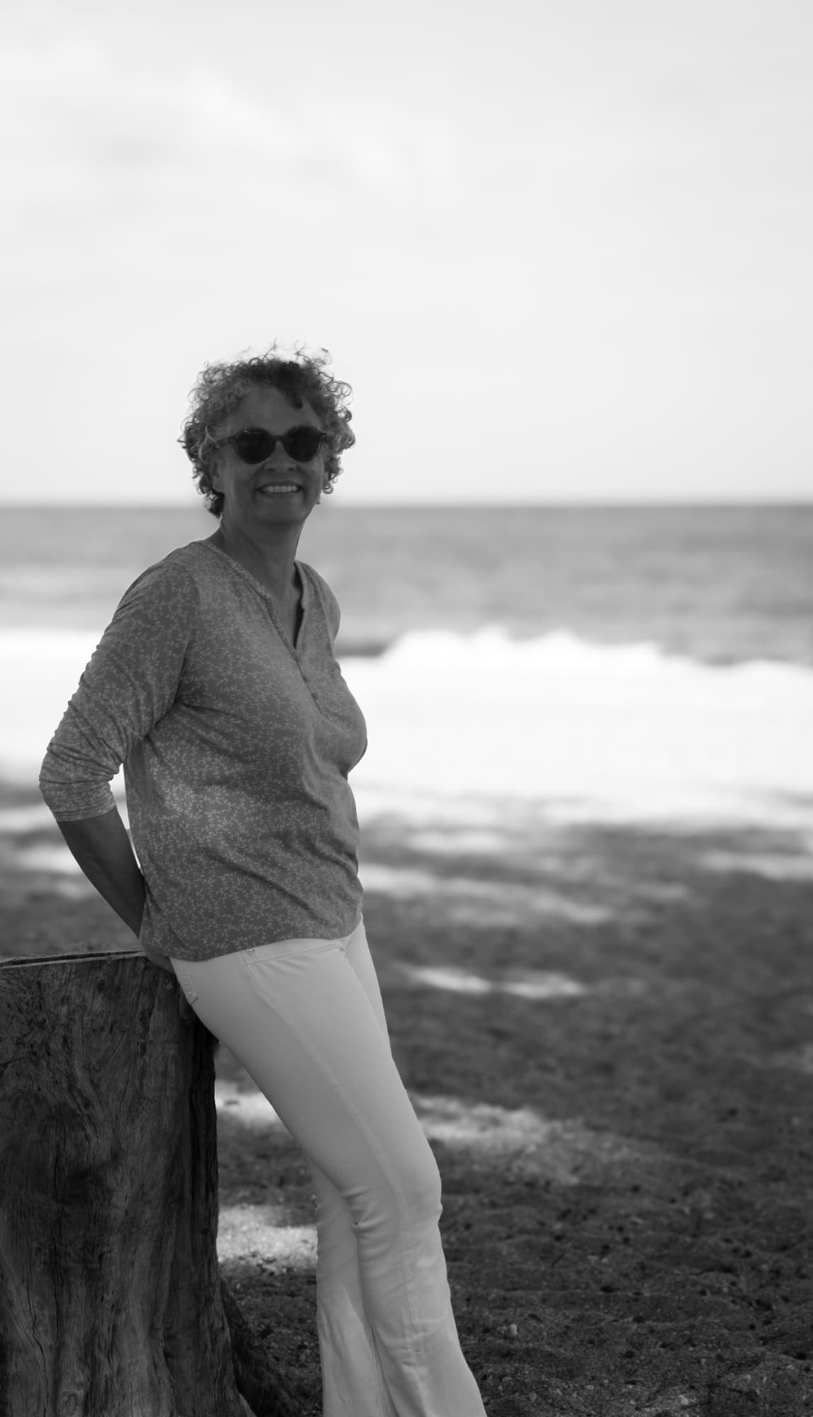 Valérie Patole adossée à un tronc sur la plage, en noir et blanc